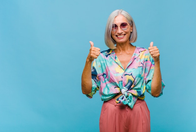 Mujer fresca de mediana edad sonriendo ampliamente luciendo feliz, positiva, segura y exitosa, con ambos pulgares hacia arriba