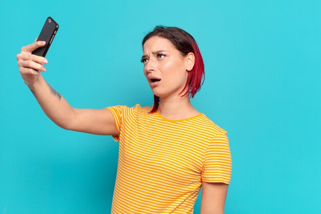 Mujer fresca de pelo rojo usando un teléfono inteligente.