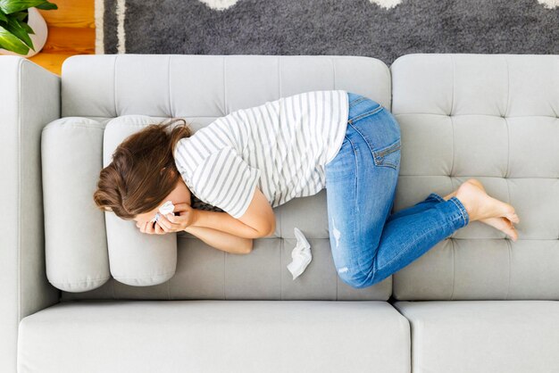 Mujer frustrada cubriendo la cara y llorando acostada en el sofá en casa sola