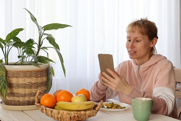 Mujer con fruta y teléfono inteligente en la mesa.