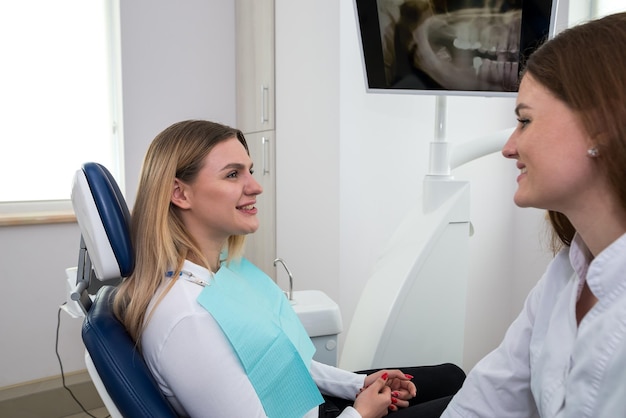 La mujer fue al dentista. Está sentada en la silla del dentista. El dentista explica y aconseja al paciente. Una dentista en un consultorio dental está hablando con un paciente y preparándose para el tratamiento.