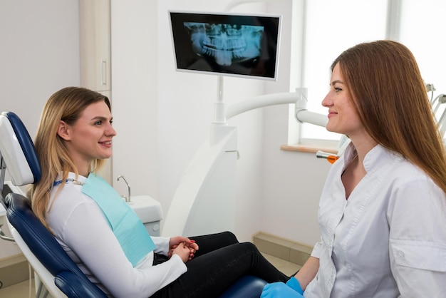 La mujer fue al dentista. Está sentada en la silla del dentista. El dentista explica y aconseja al paciente. Una dentista en un consultorio dental está hablando con un paciente y preparándose para el tratamiento.