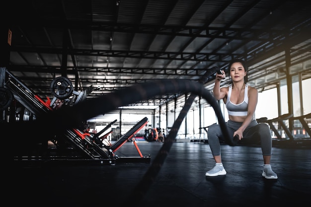 Mujer fuerte asiática haciendo ejercicio con cuerdas de batalla Un entrenamiento femenino solo en el gimnasio