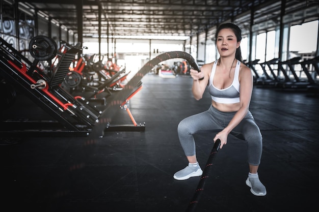 Mujer fuerte asiática haciendo ejercicio con cuerdas de batalla Un entrenamiento femenino solo en el gimnasio