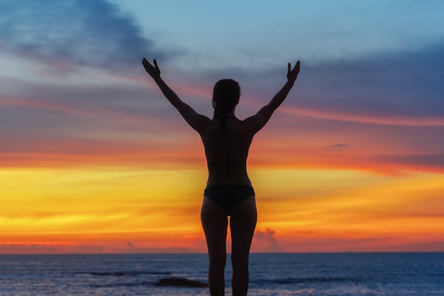 Mujer fuerte confianza abre los brazos bajo el amanecer en la playa