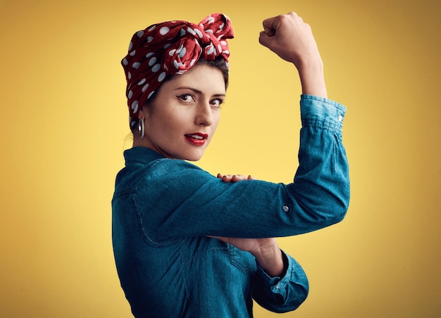 Foto mujer fuerte y flexionando músculo retrato de una chica pinup en estudio por poder de belleza y moda persona femenina muestra bíceps sobre un fondo amarillo para motivación libertad y estilo retro o vintage