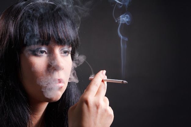 Mujer fumadora con humo de cigarrillo sobre fondo negro