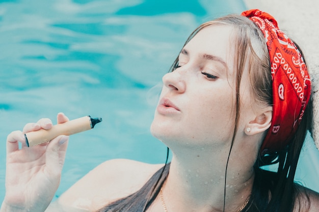 Mujer fumando con cigarrillo electrónico. Mujer joven fumar cigarrillo electrónico en la piscina al aire libre