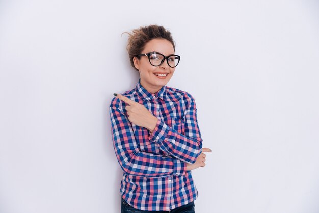 Mujer con gafas y camisa a cuadros apuntando hacia afuera