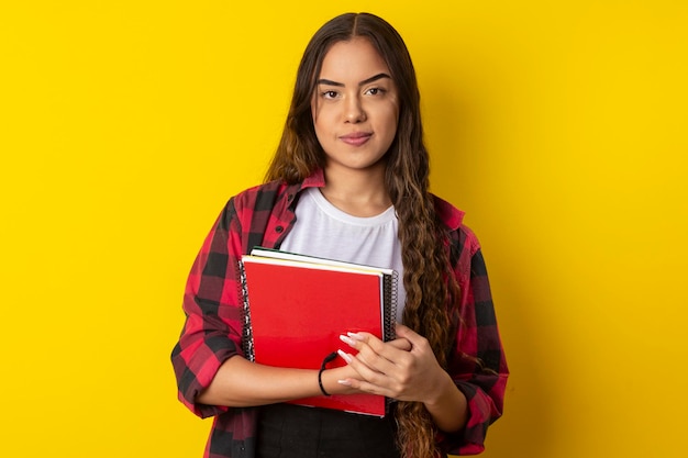 Mujer con gafas camisa a cuadros sosteniendo libros y cuaderno con una mochila en la espalda