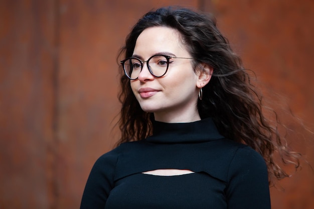 Una mujer con gafas se para frente a una pared roja.