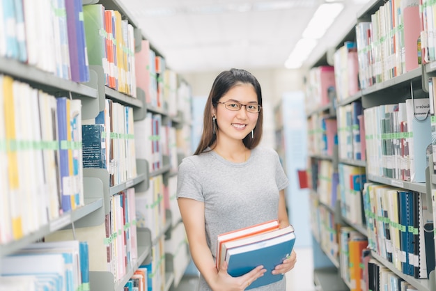 Mujer con gafas con libro en la biblioteca.