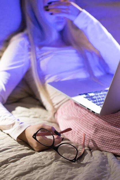 Foto mujer con gafas en la mano se queda dormida después de trabajar hasta tarde en la noche en la computadora portátil frotando los ojos