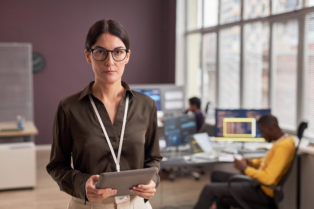 Mujer con gafas mirando a la cámara mientras está de pie en la oficina de desarrollo de TI