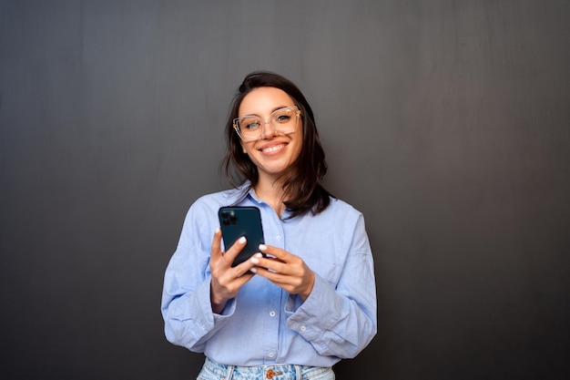 Mujer con gafas posa con el teléfono aislado sobre un fondo negro