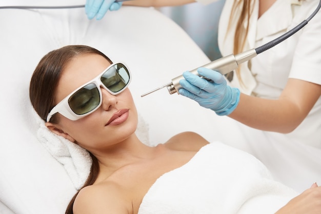 Mujer con gafas de protección recibiendo tratamiento facial con láser