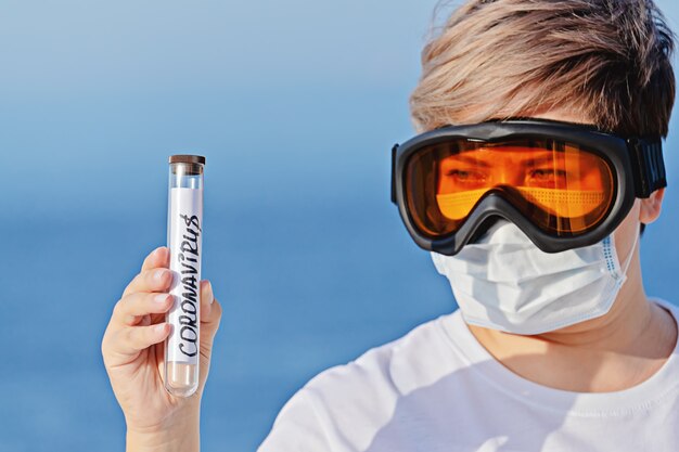 Mujer con gafas protectoras y mascarilla quirúrgica sostiene en el tubo de laboratorio de mano