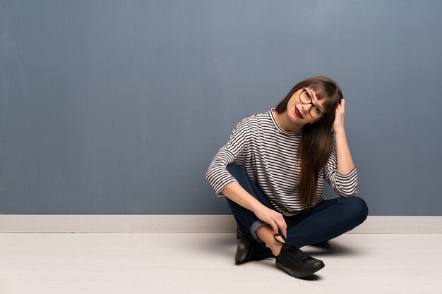 Mujer con gafas sentada en el suelo con gafas y sonriendo