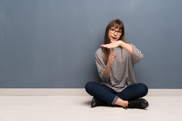 Mujer con gafas sentada en el suelo haciendo gesto de tiempo