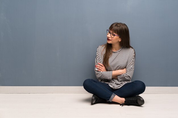 Foto mujer con gafas sentada en el suelo mirando hacia el lado