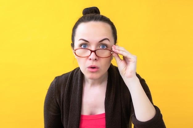 Mujer con gafas sobre un fondo amarillo con dudas en su rostro