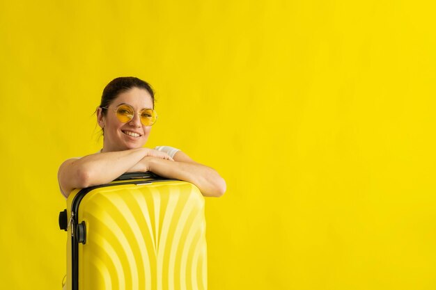 Foto una mujer con gafas de sol abraza una maleta con un fondo amarillo