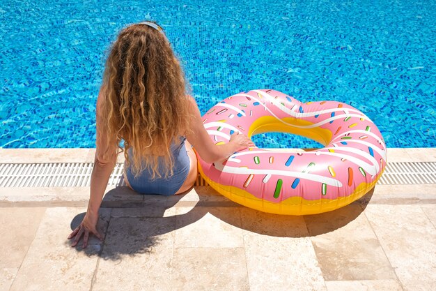 mujer en gafas de sol donut inflable junto a la piscina en el resort.