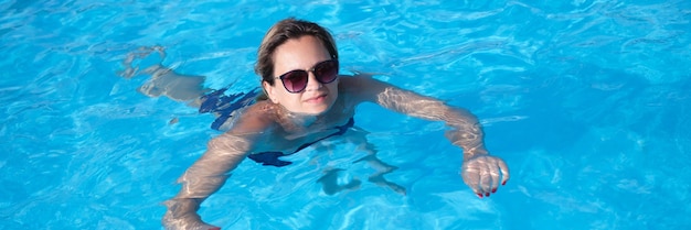 Mujer con gafas de sol nada en la piscina en verano