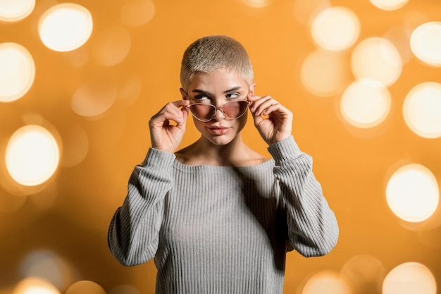 Foto mujer con gafas de sol de pie cerca del telón de fondo bokeh naranja