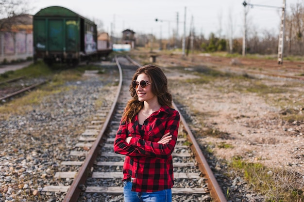 Foto mujer con gafas de sol de pie en la vía del ferrocarril