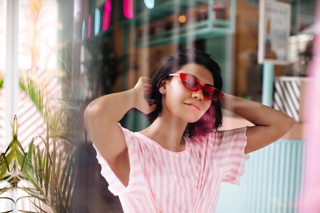 Mujer con gafas de sol rosas posando con los ojos cerrados Toma al aire libre de una chica relajada con cabello oscuro