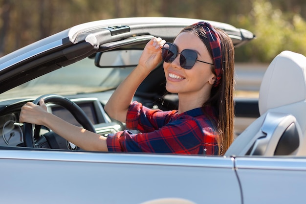 Mujer con gafas de sol sentada en convertible y sonriendo a la cámara