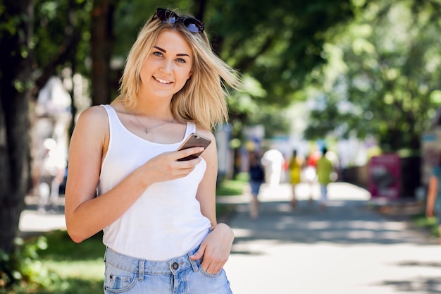 Mujer con gafas de sol sonriendo mientras tiene un móvil en la mano