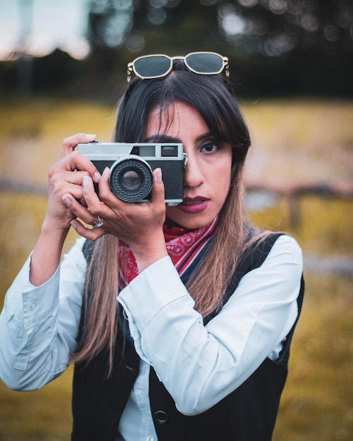 Mujer con gafas de sol tomando fotos con cámara analógica