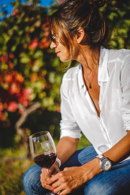 Foto mujer con gafas de sol con vino rojo contra las plantas