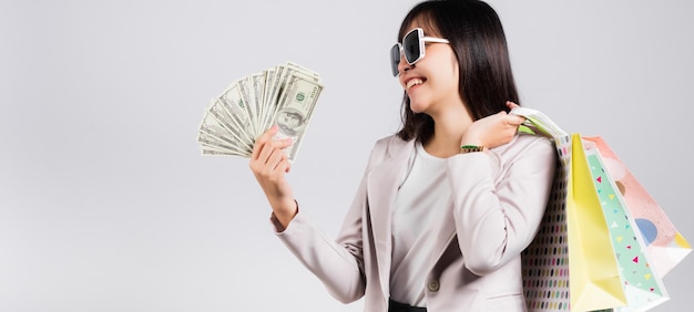 Mujer con gafas sonrisa de comprador seguro sosteniendo bolsas de compras en línea multicolor y billetes de dinero en dólares en la mano