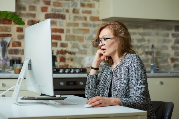 Una mujer con gafas trabaja remotamente en una computadora de escritorio en su estudio. Una empleada sorprende a los jefes en una videoconferencia en casa. Una profesora preparándose para una conferencia en línea.