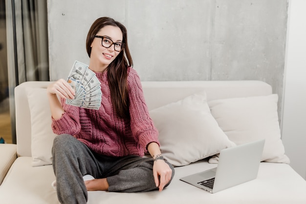 Mujer ganando dinero en casa en un sofá con laptop