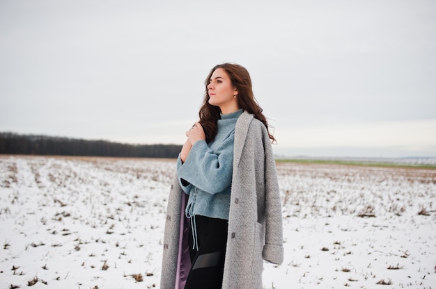 Mujer gentil en abrigo gris contra el paisaje de nieve.