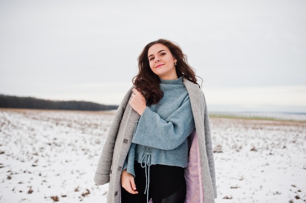 Mujer gentil en abrigo gris contra el paisaje de nieve.