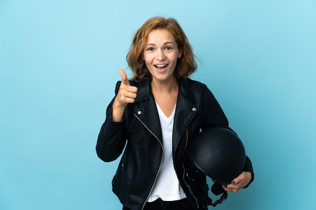 Mujer georgiana sosteniendo un casco de motocicleta aislado en la pared azul sorprendido y apuntando hacia el frente