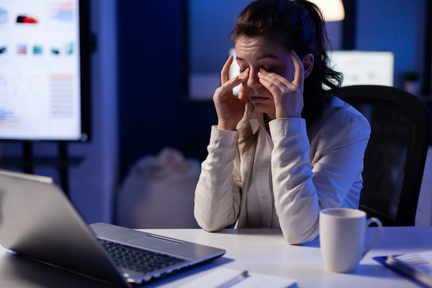 Mujer gerente estresada masajeando los ojos cansados mientras está sentado en el lugar de trabajo en la oficina de puesta en marcha trabajando