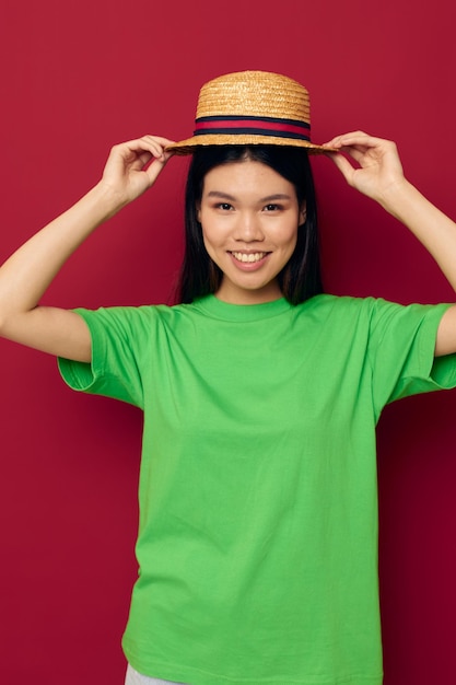 Mujer con gestos de apariencia asiática con las manos con un sombrero en un estilo de vida de camiseta verde inalterado