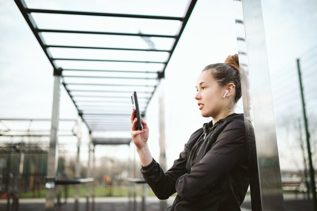 Foto mujer en gimnasio al aire libre con auriculares y smartphone.