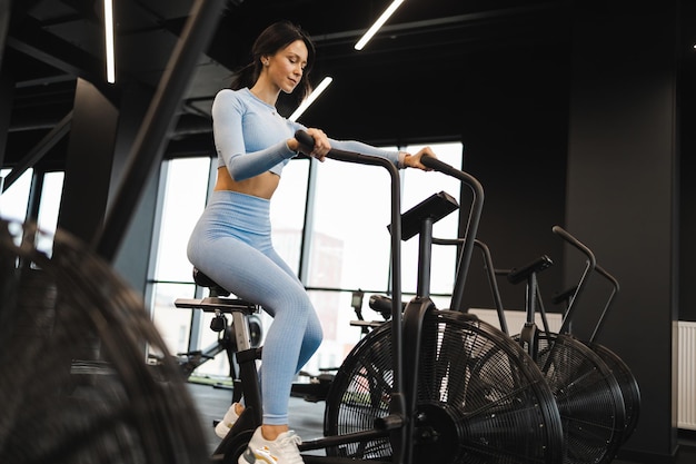 Mujer en el gimnasio crossfit con bicicleta estática para ejercicios cardiovasculares