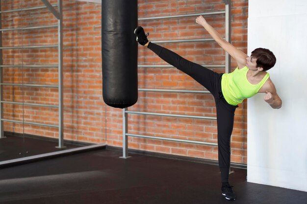 Mujer en el gimnasio patea un pie en un saco de boxeo