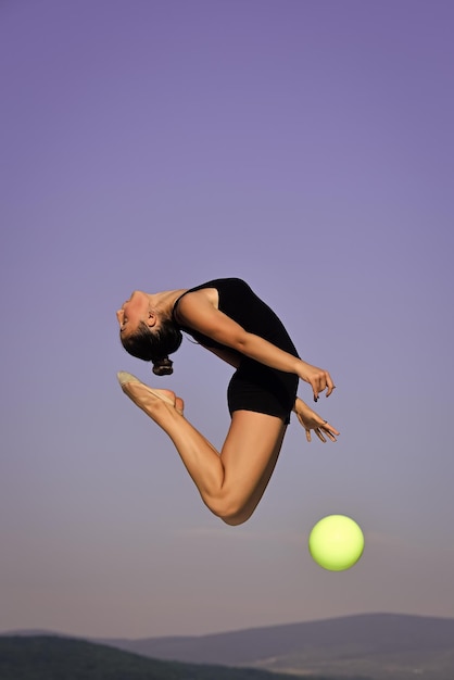 Mujer gimnasta con bola verde sobre fondo de cielo azul