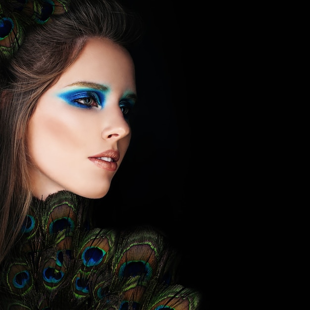 Mujer glamorosa con maquillaje y plumas de pavo real sobre fondo negro