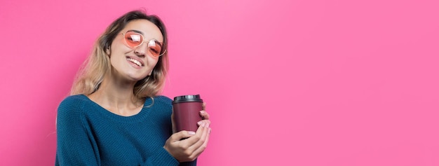 Mujer de glamour en vasos con un suéter azul con un trago de café sobre un fondo rosa