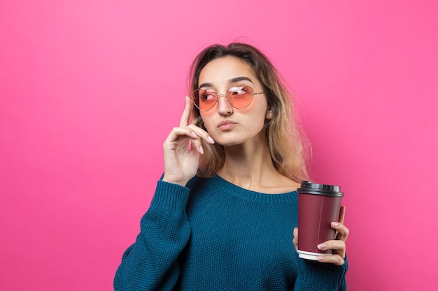 Mujer de glamour en vasos con un suéter azul con un trago de café sobre un fondo rosa